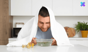 Mężczyzna z ręcznikiem na głowie, trzymający miskę z gorącą wodą, domowe leczenie oskrzeli.